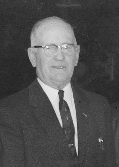Elderly man smiling, wearing glasses and suit.