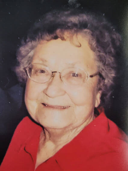Smiling elderly woman wearing glasses and a red shirt.