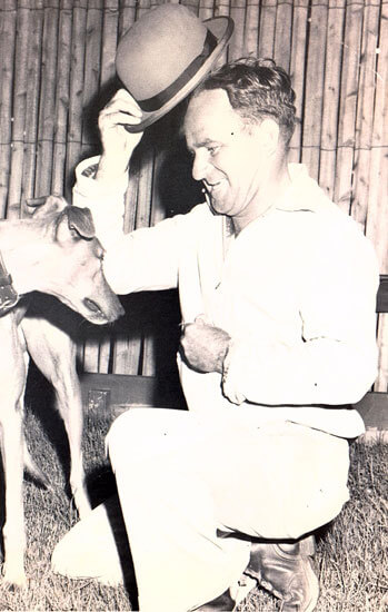 Man tipping hat to a greyhound dog.