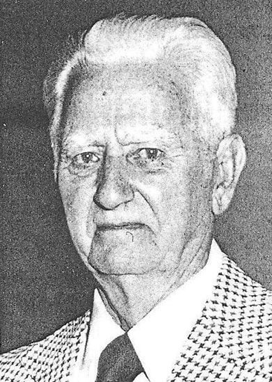 blair-merrill Elderly man wearing checkered suit, looking serious.