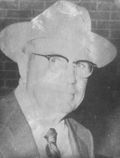 Elderly man in suit and hat, smiling slightly.