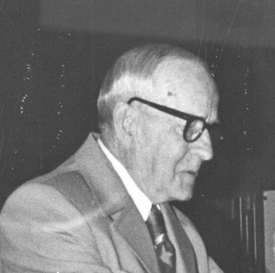 Elderly man with glasses, dressed in a suit.