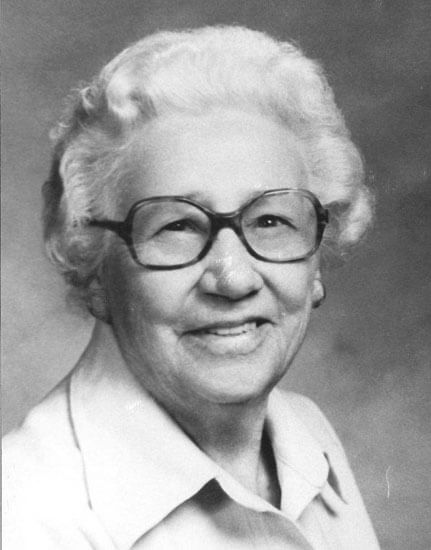 Elderly woman with glasses smiling warmly.