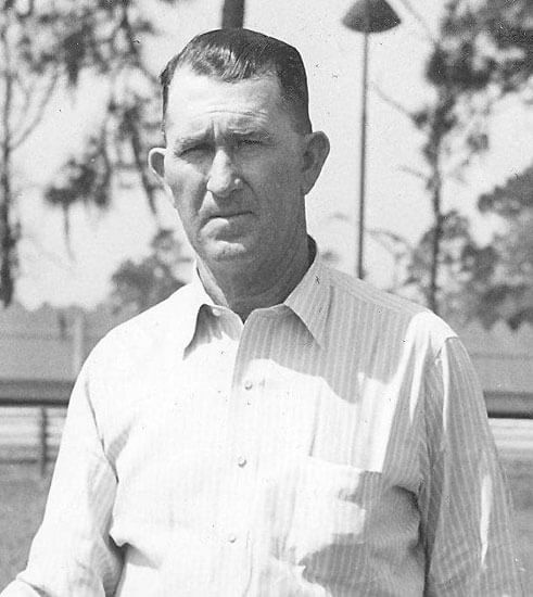 Man standing outdoors, wearing a striped shirt, stern expression.