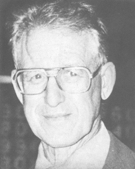 Elderly man with glasses smiling gently.