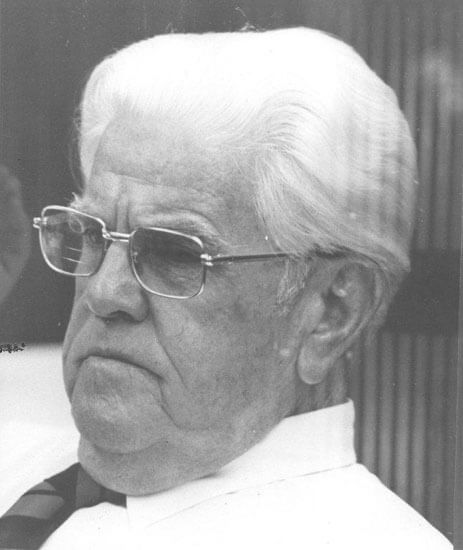 Elderly man with glasses looking thoughtfully to the side.