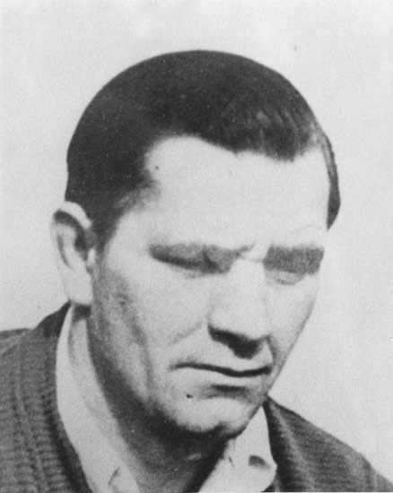 Man with serious expression, looking downward. Black-and-white photo.