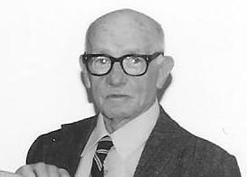 Elderly man with glasses wearing suit and tie.