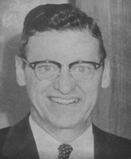 dewhurst-clint Smiling man wearing glasses in a formal suit.