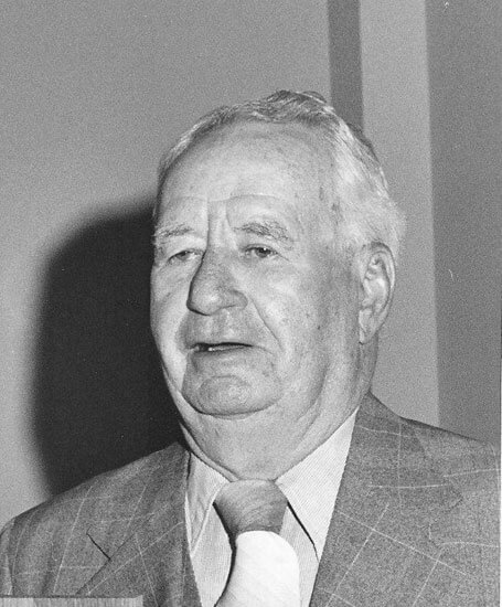 Elderly man in suit, looking forward attentively.