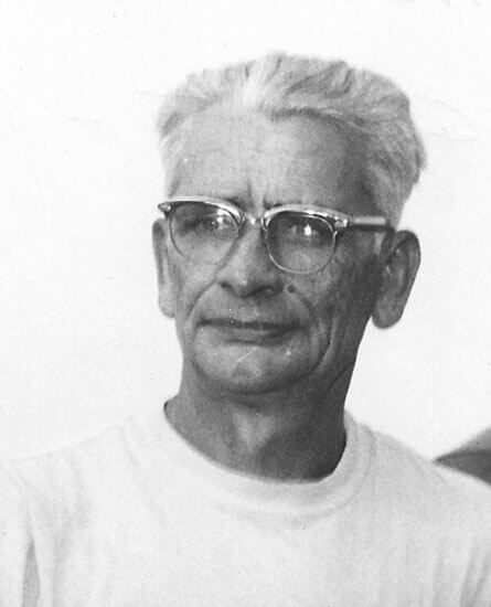 Elderly man with glasses gazing thoughtfully ahead.