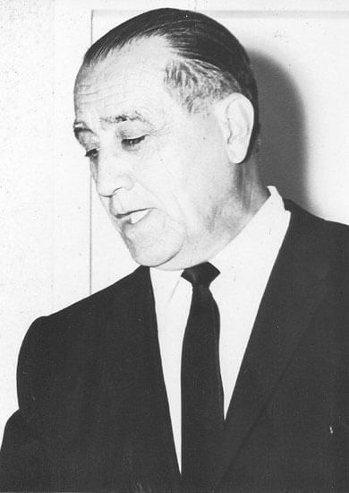 Elderly man in suit looking downward thoughtfully.