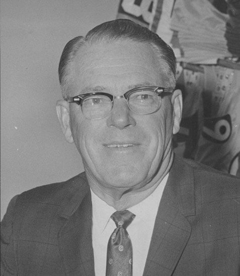 Smiling man in suit and glasses, sitting indoors.