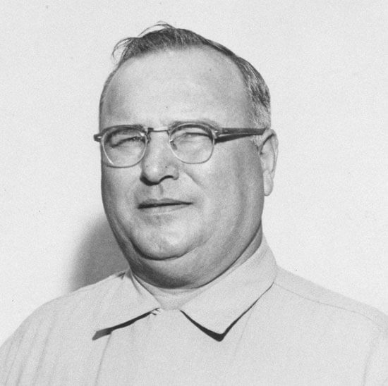 Man wearing glasses, looking serious, in grayscale portrait.