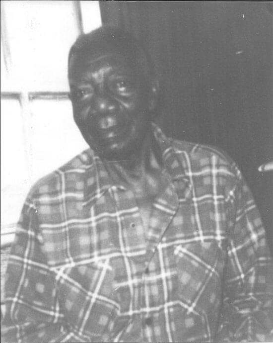 Elderly person in plaid shirt, sitting indoors.