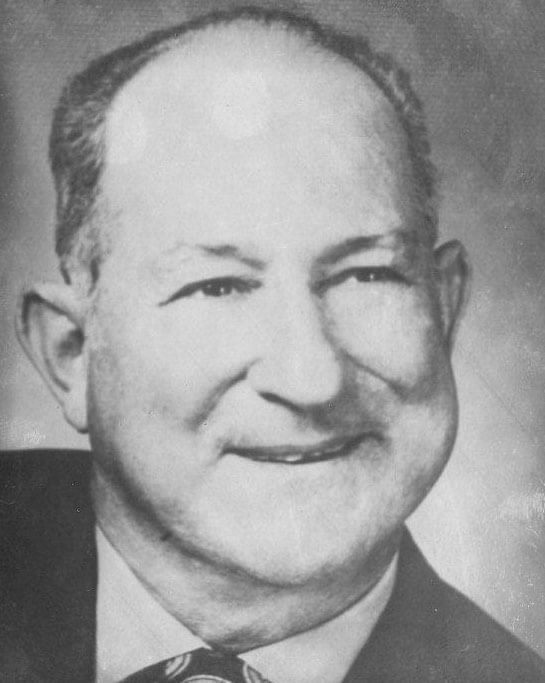 Smiling man in formal attire, grayscale photograph.