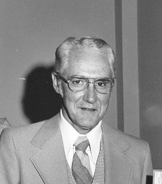Elderly man smiling, wearing a suit and tie.