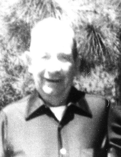 Smiling person outdoors, wearing a dark collared shirt.