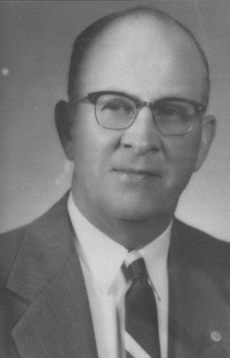 Man in suit with glasses, serious expression.