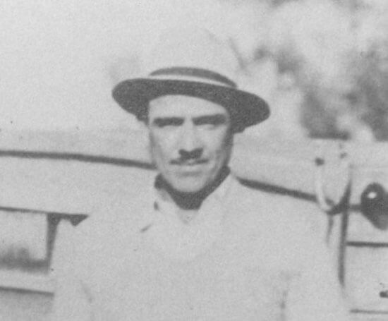 Man in hat standing by wooden fence.