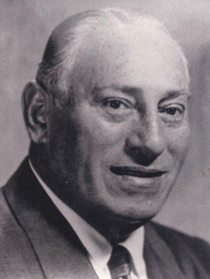 Man in suit smiling softly, vintage black-and-white portrait.