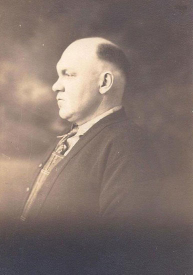 Bald man in profile, wearing a suit.