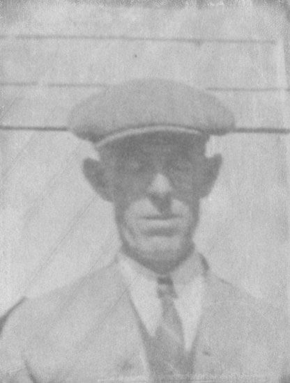 mchugh-bill Man wearing flat cap, suit, and tie, facing forward.