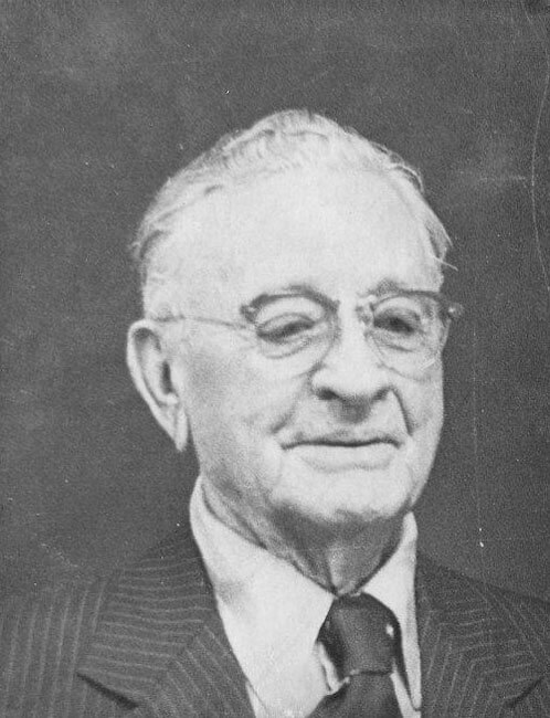 Elderly man smiling in formal attire.