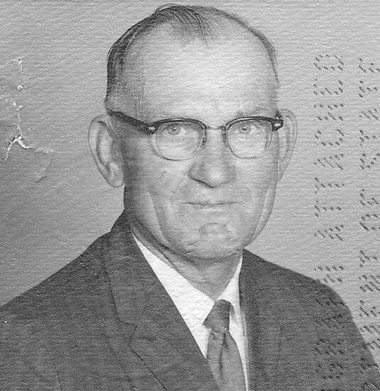 Elderly man wearing glasses, suit, and tie.
