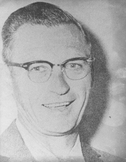 Smiling man wearing glasses in a grayscale photo.