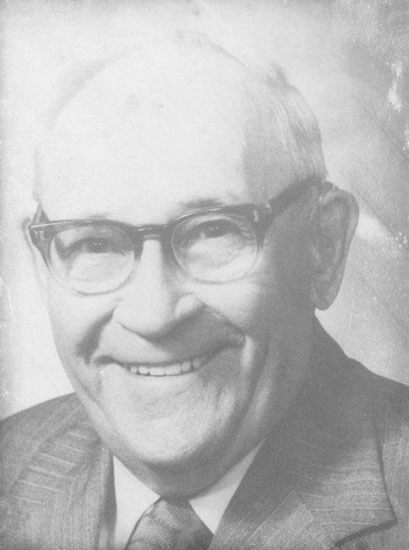 shugart-hw Smiling man wearing glasses and a suit.