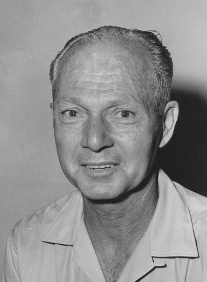 Elderly man smiling slightly, wearing a collared shirt.
