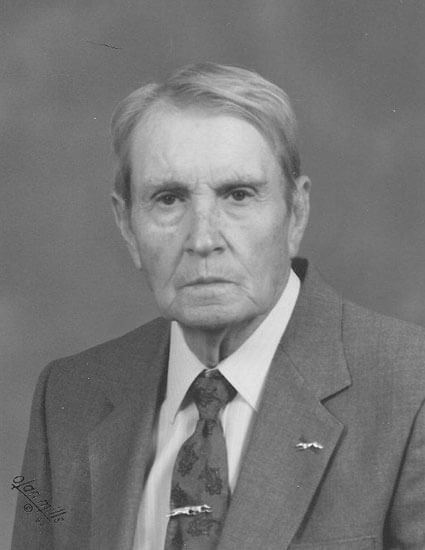 Elderly man in suit, expression serious, grayscale portrait.