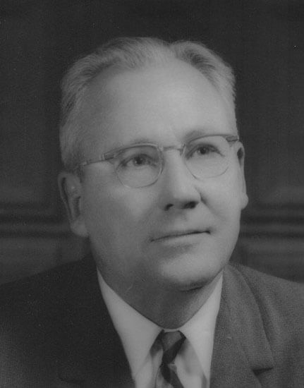 Man in suit, wearing glasses, looking upwards thoughtfully.