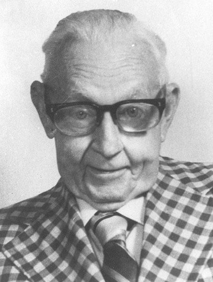 Elderly man smiling in plaid jacket and glasses.